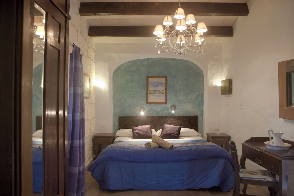 A bedroom with a large bed, a chandelier, a wooden headboard, and a painting on the wall.