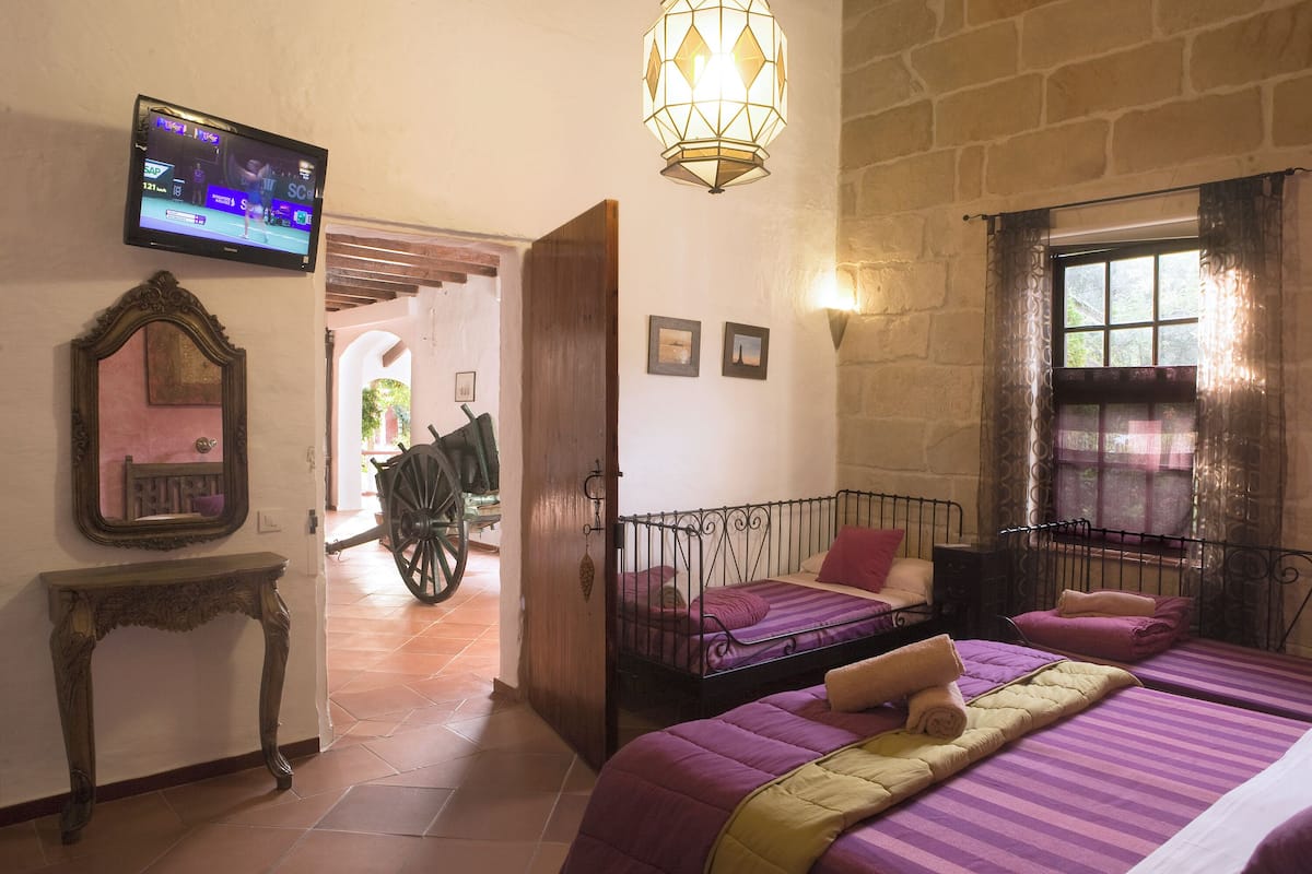 A room with two beds, a television, a mirror, and a wooden cart in the background.