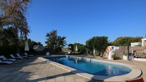 A swimming pool with lounge chairs and umbrellas, surrounded by stone walls and greenery. - Matchani Gran (Mahón)