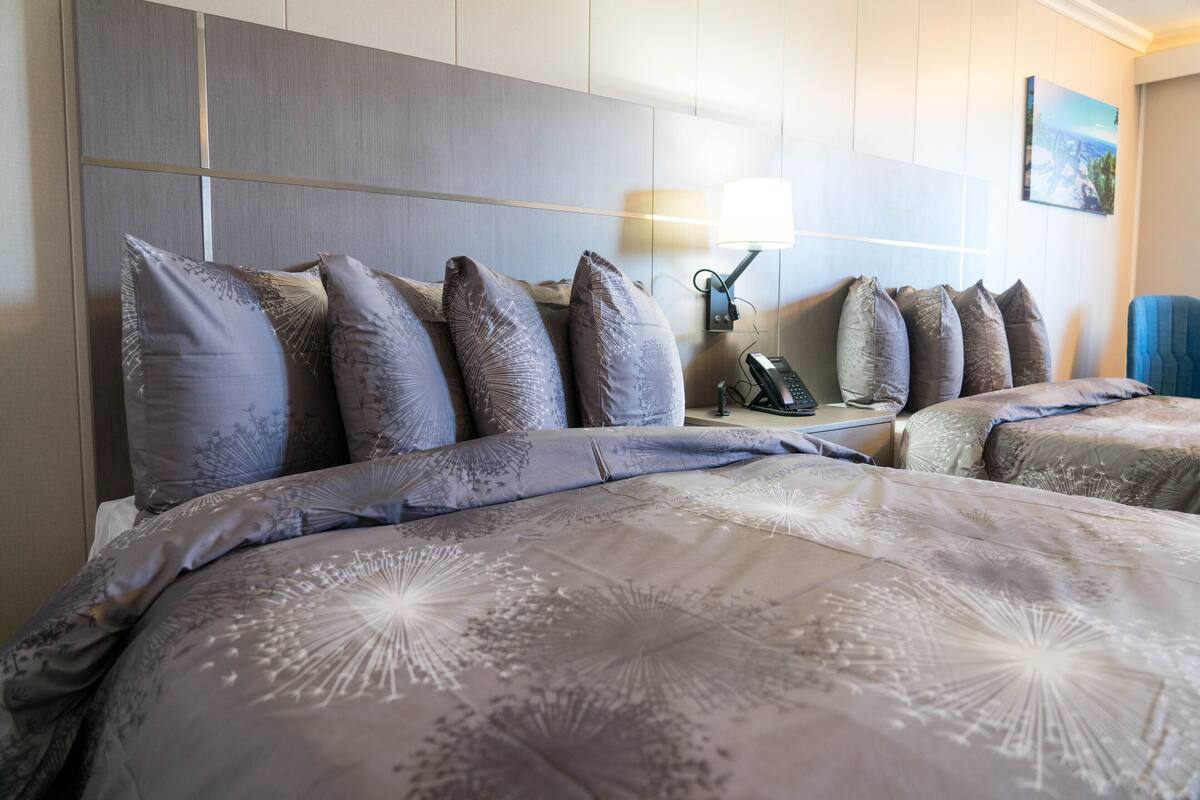 A hotel room with a large bed, multiple pillows, a bedside table with a lamp, and a chair.