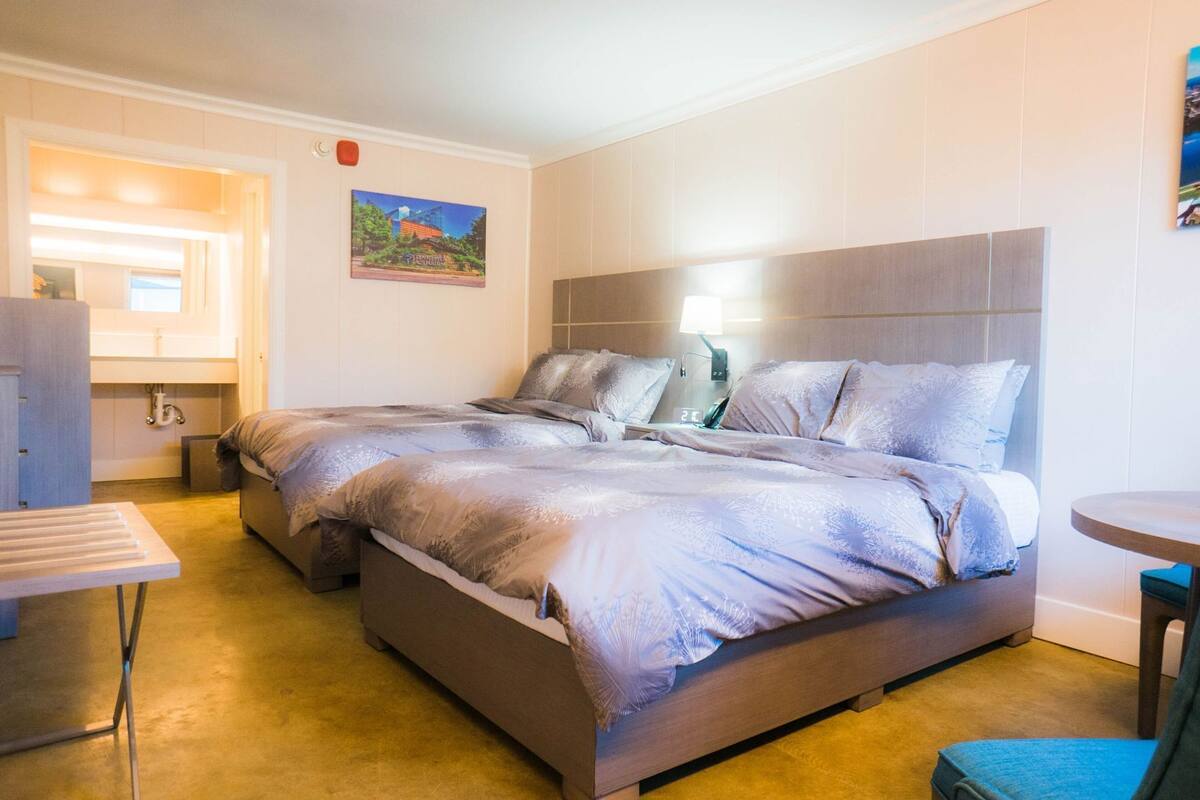 A hotel room with a large bed, a bedside table, a small table, and a painting on the wall.