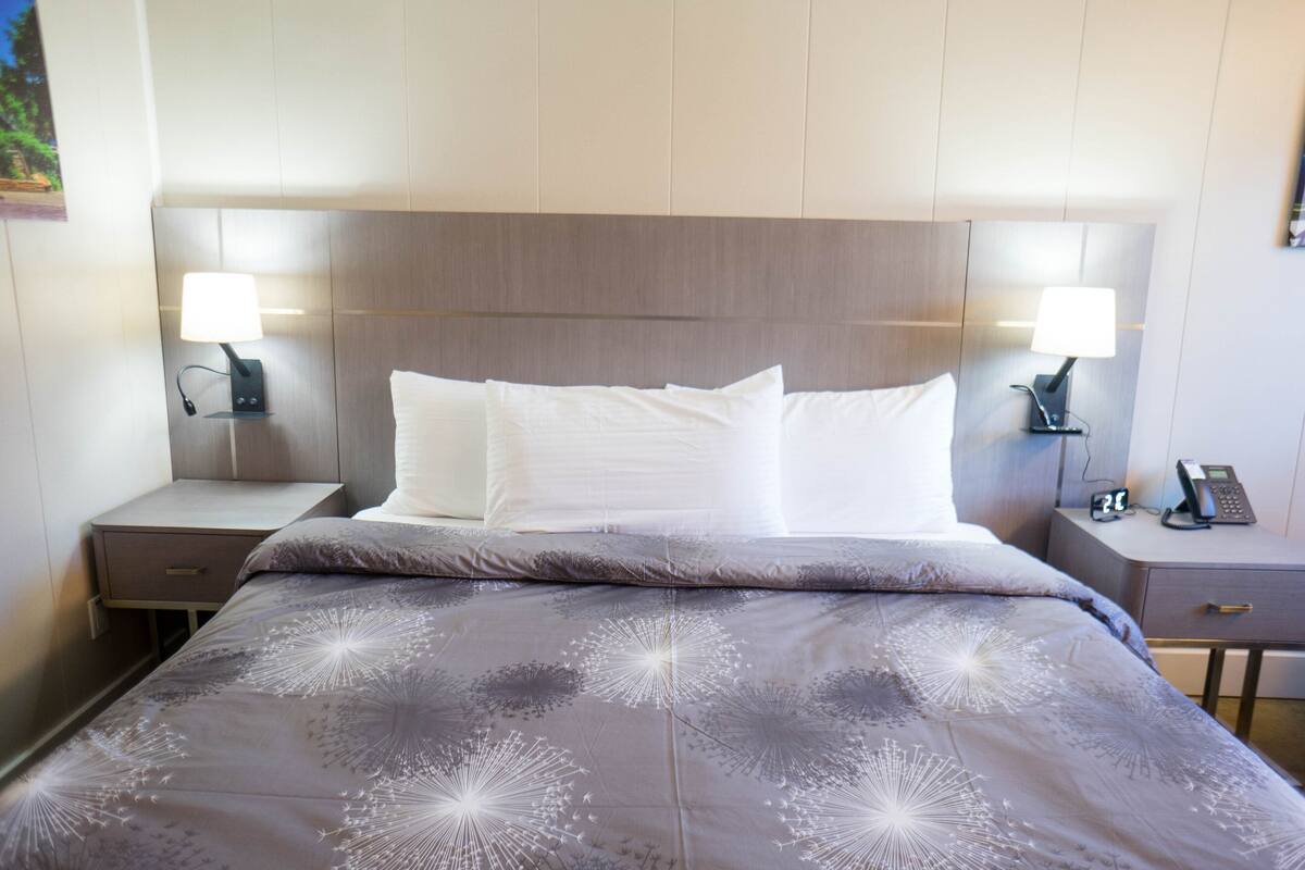 A hotel room with a bed, two bedside tables, a nightstand, a lamp, and a phone.