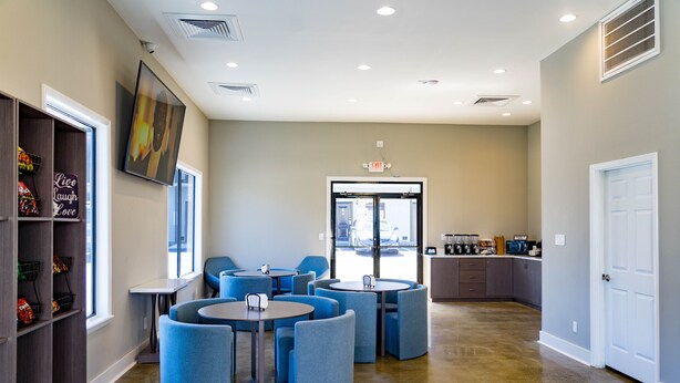 A modern interior with round tables and blue chairs, a kitchen area, and a door with an exit sign. - Stay Express Inn Chattanooga (Chattanooga)