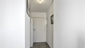 Un corridoio stretto con una porta bianca in fondo, pavimento piastrellato e una lampada a soffitto.
