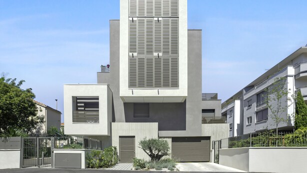 Un edificio moderno con una torre centrale, due ali laterali e un ingresso carrabile.