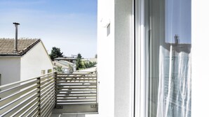 Un balcone con ringhiera in metallo, vista libera sul quartiere e un edificio con tetto in tegole sullo sfondo.
