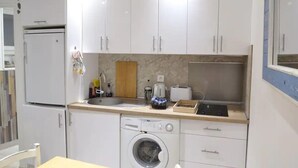 Pieni, käytännöllinen keittiö, jossa on valkoiset kaapit, pesukone, pesuallas ja leivänpaahdin.