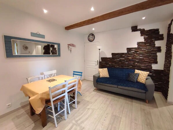 A dining area with a table and chairs, a sofa, a wall clock, and a decorative wall.