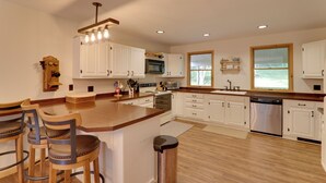 A modern kitchen with white cabinets, a wooden island with bar stools, stainless steel appliances, and large windows. - 2 Mi to Elk Mountain: Poconos Escape on 11 Acres! (Union Dale)