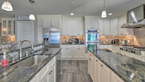 Una cocina moderna con armarios blancos, encimeras de granito, electrodomésticos de acero inoxidable e iluminación colgante.