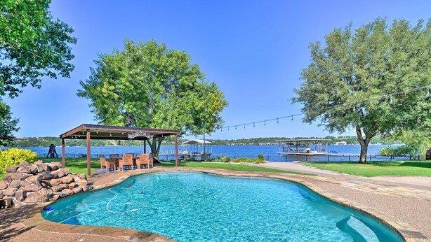 Piscina con pérgola y sillas, rodeada de árboles y vistas a un lago.