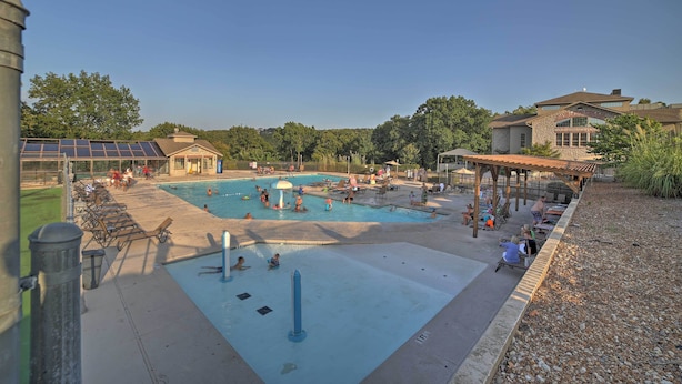 A swimming pool area with lounge chairs, a covered seating area, and a building with a stone facade. - Watefront Branson Condo w/ Screened-In Balcony! (Branson)