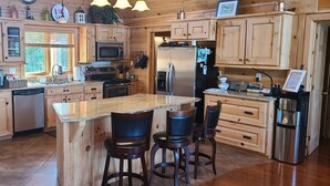 A wooden cabin-style kitchen with a granite island, bar stools, stainless steel appliances, and a large window. - Where Luxury and Tranquility Meet (Whitbourne)