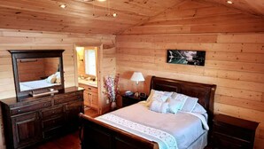 A wooden cabin bedroom with a bed, dresser, mirror, and a wall-mounted picture. - Where Luxury and Tranquility Meet (Whitbourne)
