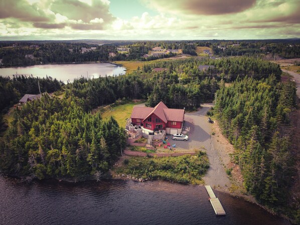 An aerial view of a cabin surrounded by dense forest and a lake, with a dock extending into the water. - Where Luxury and Tranquility Meet (Whitbourne)