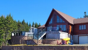 A two-story log cabin with a large deck, a garage, and a staircase leading to the upper level. - Where Luxury and Tranquility Meet (Whitbourne)
