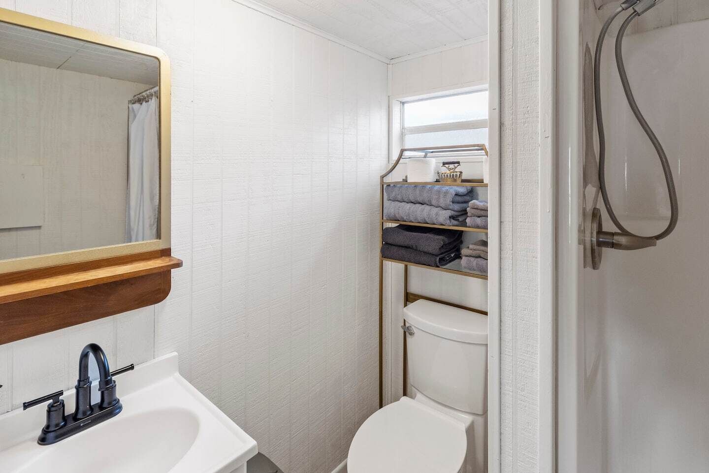 A compact bathroom with a white sink, a mirror, a toilet, and a shower.
