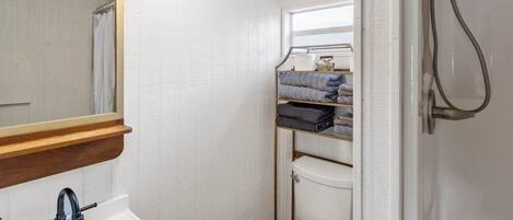 A compact bathroom with a white sink, a mirror, a toilet, and a shower.