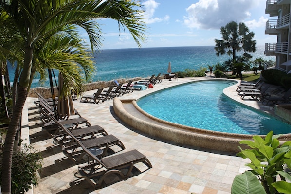 A pool area with lounge chairs and a view of the ocean.