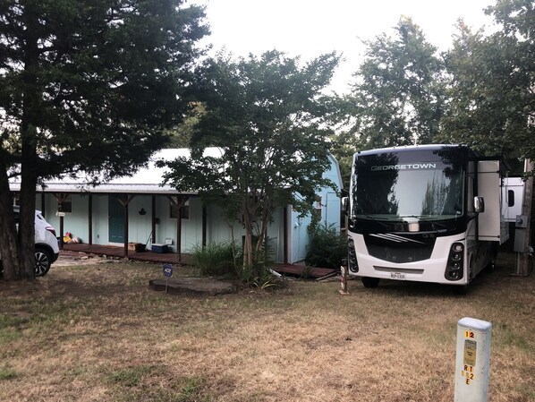 A recreational vehicle (RV) parked in a grassy area with a covered structure in the background. - Juniper Cabin--wildlife w/ serene patio and outdoor experience--30/50 amp hookup (Canadian)