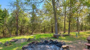 A campsite with a fire pit surrounded by rocks, picnic tables, and a wheelbarrow.