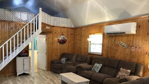 A wooden interior with a staircase, a sofa set, a small cabinet, and an air conditioning unit.