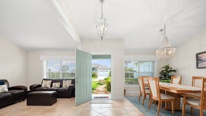 A spacious living room with a sofa set, a dining area with a wooden table and chairs, and a view of the outside. - Complete Searenity by Distinctive Beach Rentals (Palm Coast)