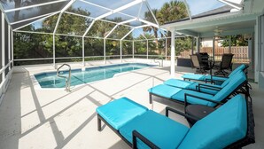 A covered outdoor pool area with a clear view of the pool, lounge chairs, and surrounding greenery. - Complete Searenity by Distinctive Beach Rentals (Palm Coast)