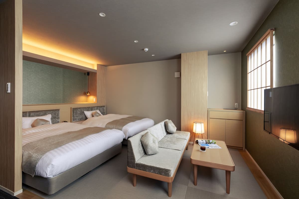 A hotel room with two beds, a sofa, a small table, and a TV.