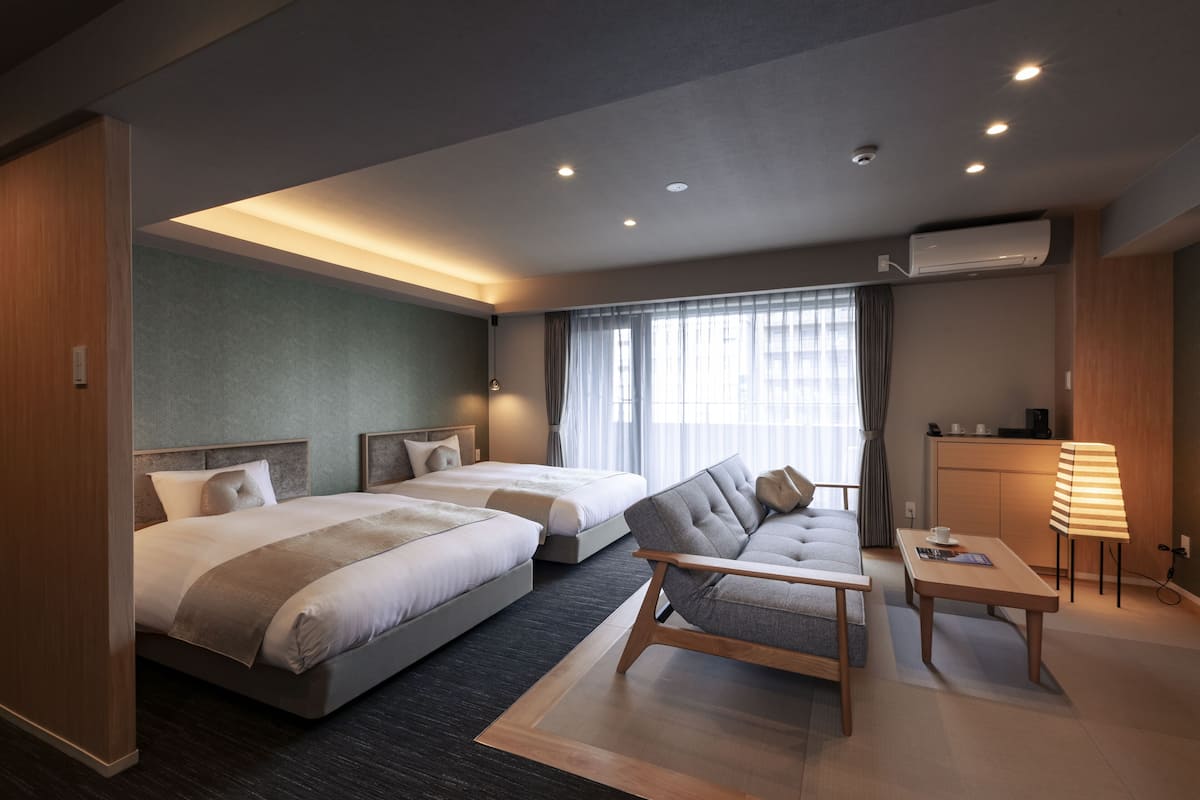 A modern hotel room with two beds, a sofa, a small table, and a desk.