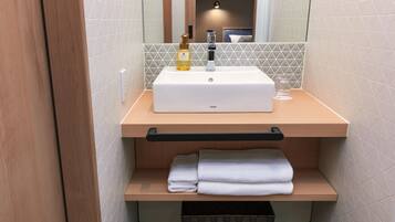A bathroom with a white sink, a bottle of hand soap, and neatly folded towels on a wooden shelf.