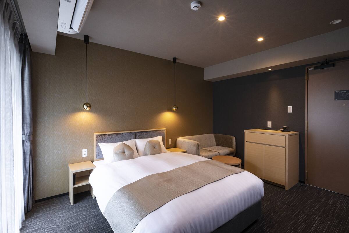 A modern hotel room with a large bed, a desk, a chair, and a wardrobe.
