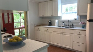 A kitchen with white cabinets, a stainless steel refrigerator, a sink, and a window with a view of greenery.