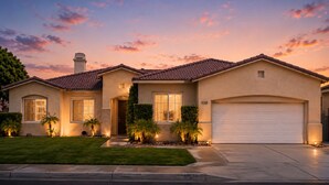 A two-story house with a garage, a well-maintained lawn, and a sunset sky. - Home Theater, Arcade games, Water Slide, Lagoon-Style Pool & Extra-Large Spa (Indio)