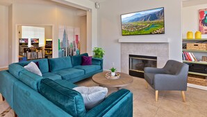 A modern living room with a teal sofa, a grey armchair, a coffee table, and a fireplace. - Home Theater, Arcade games, Water Slide, Lagoon-Style Pool & Extra-Large Spa (Indio)