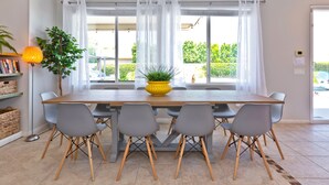 A dining area with a wooden table, grey chairs, a yellow plant, and a bookshelf with books and baskets. - Home Theater, Arcade games, Water Slide, Lagoon-Style Pool & Extra-Large Spa (Indio)