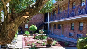 Un patio con un edificio de ladrillo, un árbol y una fuente.