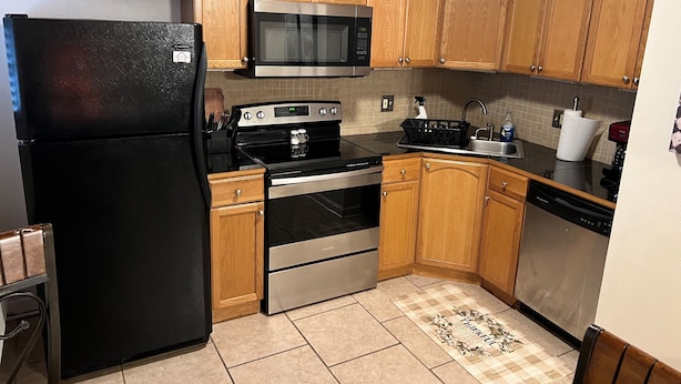 Una cocina con armarios de madera, un refrigerador negro, microondas, estufa y lavavajillas.