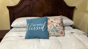 Una cama con cabecera de madera, dos almohadas decorativas y una colcha blanca.