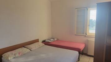 A bedroom with two beds, a window with blinds, and a hanging light fixture.