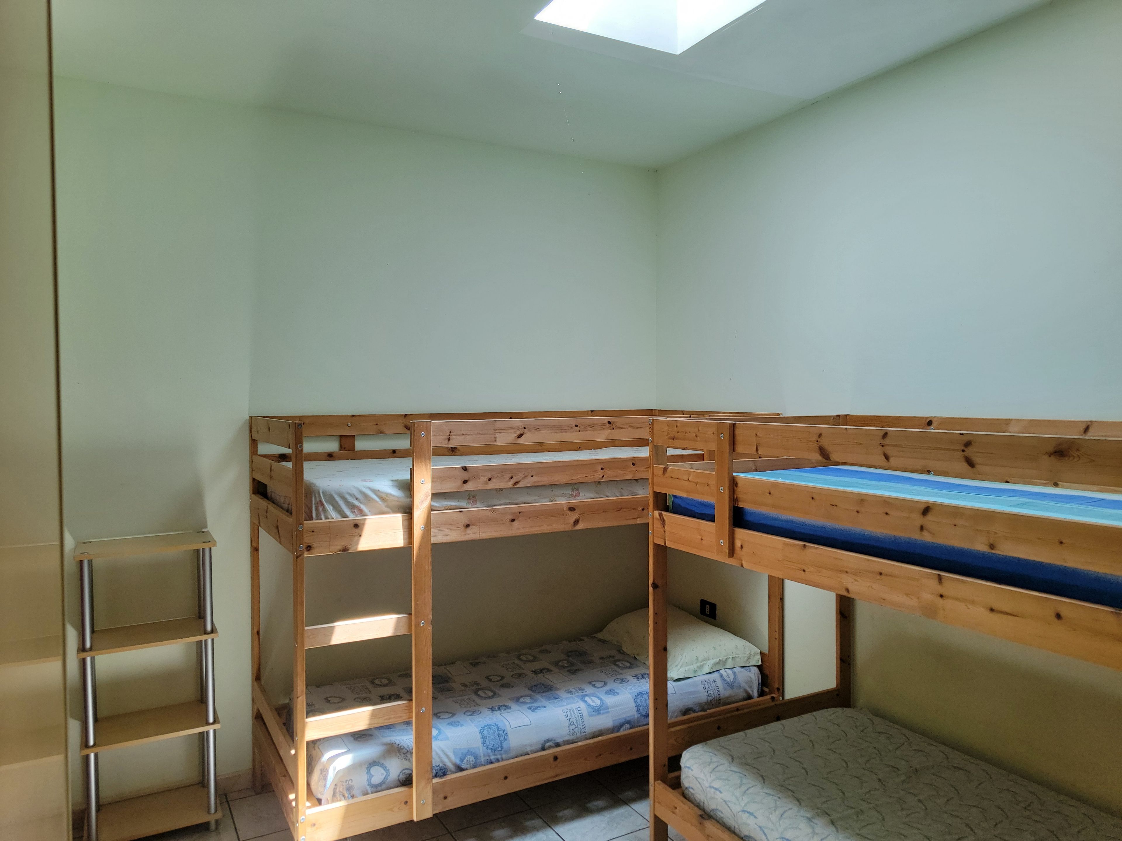 A room with bunk beds, a metal shelf unit, and a skylight.