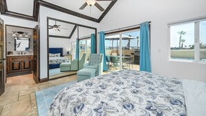 Een slaapkamer met een groot bed, een plafondventilator, een badkamer met wastafel en een balkon met zitplaatsen buiten.
