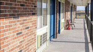 A corridor with brick walls, blue doors, and a covered walkway with a railing. - Lebo Inn (Waverly)