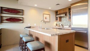 Una cucina moderna con isola centrale, sgabelli da bar, frigorifero in acciaio inossidabile e decorazioni a tema foglia sulla parete.