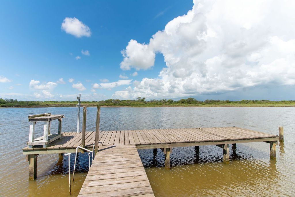 Un muelle de madera que se adentra en una masa de agua tranquila, con un banco pequeño y una barandilla en un extremo.