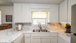 A kitchen with white cabinets, a marble countertop, a sink, and a window with blinds. - "Peace At Bay" - Home on Caney Creek, Just Minutes to ICW, Gulf & Sargent Beach (Bay City)