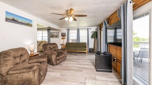 A living room with a ceiling fan, a sofa, a TV stand, and a window with curtains. - "Peace At Bay" - Home on Caney Creek, Just Minutes to ICW, Gulf & Sargent Beach (Bay City)