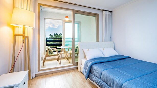 Un dormitorio con cama, mesita de noche, lámpara y vistas a un balcón con mesa y sillas.