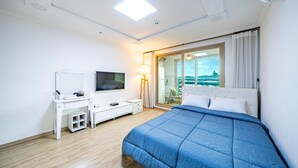 Habitación de hotel con cama, escritorio con televisor, lámpara y vistas al exterior.