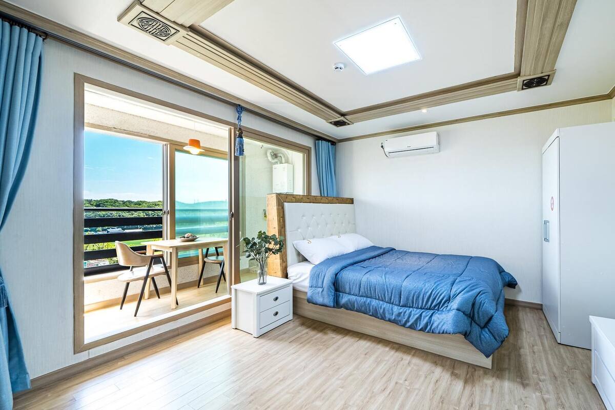A bedroom with a bed, a desk, and a view of the outdoors.